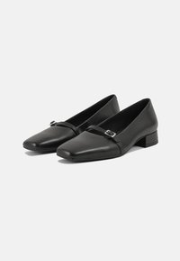 Chaussures noires en cuir à talon bas avec un bout carré, dotées d'une fine sangle avec une boucle métallique sur le coup de pied. Texture lisse.