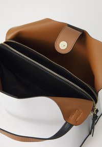 Un sac à main en cuir blanc avec des accents marron, comportant une poche zippée, un intérieur beige et des accessoires en or. Texture douce et forme distincte.
