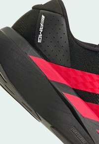 Scarpa sportiva nera con tomaia testurizzata, strisce diagonali rosa e nere, e un collarino imbottito. Branding evidente sul lato.