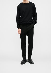 Czarny sweter z dzianiny z okrągłym dekoltem, zestawiony z czarnymi, dopasowanymi spodniami i czarnymi skórzanymi mokasynami, tworząc monochromatyczny strój.