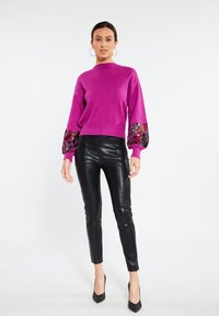 Maglione a maglia fucsia con maniche a palloncino, caratterizzato da un accento a motivo colorato, abbinato a pantaloni attillati in faux pelle neri e tacchi alti neri.