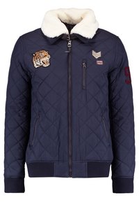 Veste matelassée bleu marine avec col en fausse fourrure blanche, écusson tigre, écussons chevron et "1980", poches zippées, et écusson "9" sur la manche.