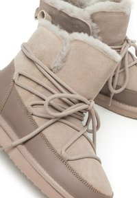 Botines de ante marrón con forro interior de piel suave, cordones flexibles y suela de goma resistente. Presentan un diseño en capas con materiales contrastantes.