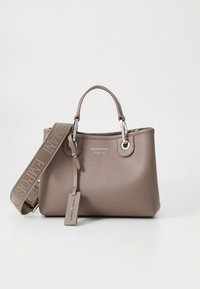 Sac à main en cuir marron avec deux poignées courtes, une bandoulière réglable, des accessoires en argent, et une petite étiquette suspendue. Présente une surface texturée.