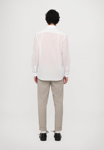 Camisa blanca de manga larga con un ajuste relajado y detalles de botones, combinada con pantalones beiges, mostrando los puños enrollados y zapatos negros.