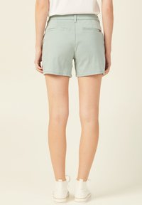 Shorts en coton vert menthe avec poches arrière et coupe décontractée, accompagnés de baskets blanches aux lacets en ruban.