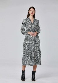Robe à motif zèbre noir et blanc avec des manches longues, un décolleté en V et une taille élastique. Portée avec des bottines noires.