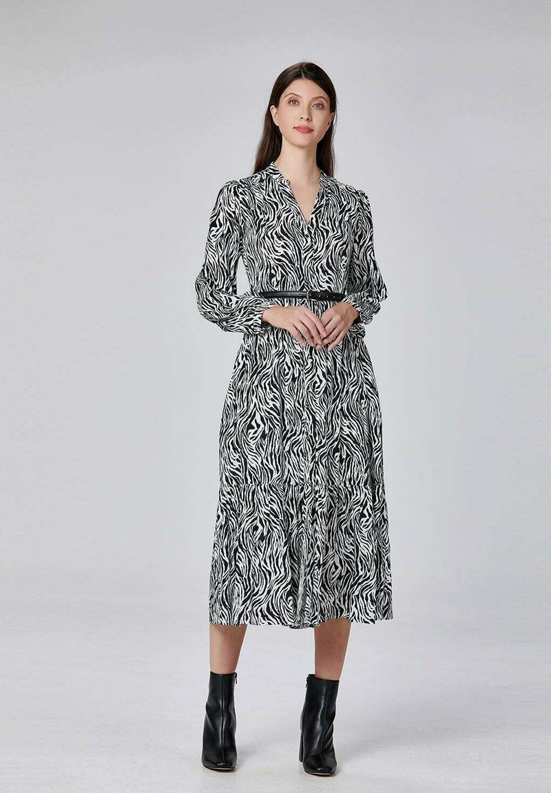 Robe à motif zèbre noir et blanc avec des manches longues, un décolleté en V et une taille élastique. Portée avec des bottines noires.