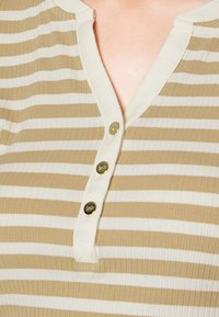 Beige och krämrandig knäppskjorta i ribbat tyg, med en placket som har tre knappar i guldton och en rund krage.