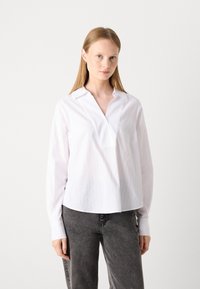 Hvit bluse med lange ermer, V-hals, vertikale striper og knappede mansjetter, kombinert med grå denimjeans. Glatt tekstur.