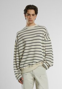 Maglione a righe in crema e blu navy, caratterizzato da scollo rotondo, veste oversize, polsini a coste e dettaglio ricamato "Proibito" sul petto.
