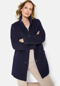 Marineblauer Wollmischmantel mit Kragen, Knopfleiste und zwei Fronttaschen. Besitzt eine weiche Oberfläche und einen lässigen Schnitt.