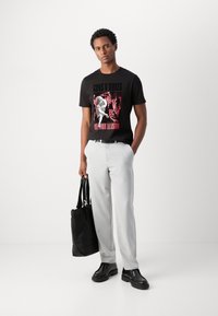 Black graphic t-shirt with a red design, paired with light gray trousers. Accessories include a black tote bag and black shoes.