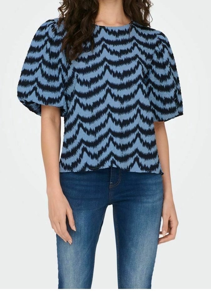 Blå blus med svart zigzag-mönster, korta puffärmar, rund halsringning och avslappnad passform. I kombination med mörkblå jeans.
