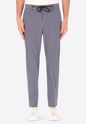 Pantaloni da uomo aderenti blu navy con motivo a fantasia e coulisse nera in vita, indossati con scarpe da ginnastica bianche.