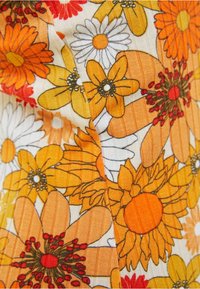 Lähikuva kuviollisesta kankaasta, jossa on keltaisia, oransseja ja valkoisia kukkia mustalla ääriviivalla kermaisella taustalla.
