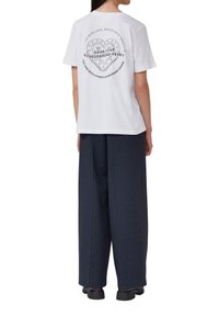 T-shirt en coton blanc avec un graphique de cœur et du texte au dos. Associé à un pantalon large à rayures noires pour un contraste.