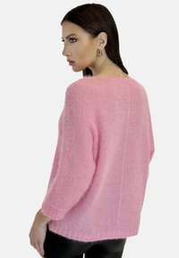 Rosa gestrickter Pullover mit lockerer Passform, Dreiviertelärmeln und weiter Ausschnitt. Die Textur ist weich und flauschig, mit gerippten Bündchen.