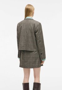 Bruine geblokte blazer met een cropped ontwerp, gecombineerd met een bijpassende rok. Heeft een lichtblauwe blouse met kraag eronder.