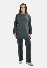 Tunika grigia a maglia con maniche lunghe e spacchi laterali, abbinata a pantaloni a vita alta coordinati con righe verticali. Sneakers bianche.