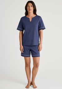 Marineblauwe shorts en set met korte mouwen gemaakt van zacht materiaal, met een V-hals en contrasterende witte afwerking op de mouwen en shorts.