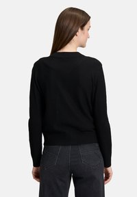 Zwarte gebreide trui met een ronde kraag en lange mouwen. Achteraanzicht, waarbij een getailleerde onderkant en minimale details worden getoond.