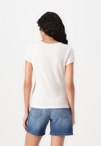 Chemise blanche à manches courtes en tissu doux. Elle a un col rond et une coupe droite, associée à un short en denim bleu avec des poches arrière.