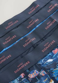 Tumedast sinine bokserite aluspesu elastse vöökohtaga, millel on heledat roosa "NEXT SIGNATURE" logo; kangal troopiline muster.
