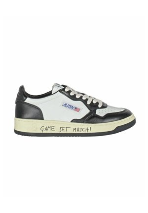 Sneaker in pelle bianca e nera con pannelli testurizzati, punta rotonda e suola in gomma. Presenta la scritta "GAME SET MATCH!" sul lato della suola.