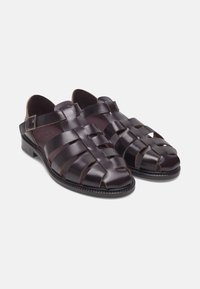 Dunkelbraune Ledersandalen mit einem geflochtenen Design, offener Zehenpartie, verstellbarem Riemen und einer strukturierten Sohle. Mit Kontrastnähten.