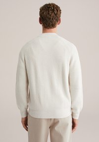 Valge kootud kampsun tekstuurse mustriga, soonilised mansetid ja alumine serv, selja vaade, vabaaja lõige, heledate pükstega.