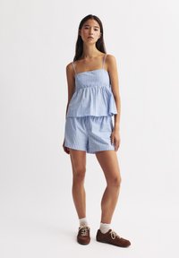 Sininen ja valkoinen raidallinen kahden osan asu, jossa on kerroksellinen peplum-toppi ohuilla hihnoilla ja vastaavat shortsit. Valmistettu kevyestä kankaasta.
