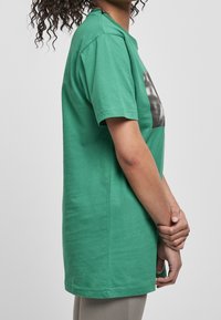 Camiseta verde de manga corta en algodón. Presenta un cuello redondo y un estampado gráfico en la parte frontal. Ajuste casual con una textura suave.