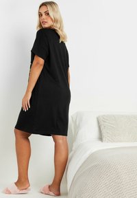 Svart knälång t-shirtklänning med korta ärmar, tillverkad av mjukt bomullstyg; matchad med rosa fluffiga tofflor.