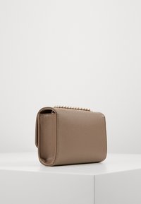 Bolso de mano texturizado en color beige con forma rectangular, que presenta un acento de cadena dorada en la parte superior. La superficie tiene un acabado de piel de melocotón.