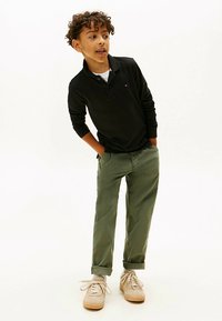 Polo de manga larga negro, pantalones de corte relajado en verde oliva y zapatillas de deporte beige. La camisa tiene cuello; los pantalones tienen puños doblados.