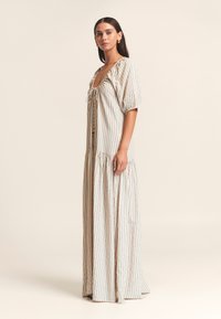 Lange, vloeiende jurk gemaakt van licht stoffen met verticale blauwe en bruine strepen, een diepe halslijn en pofmouwen. Heeft een gelaagde zoom.