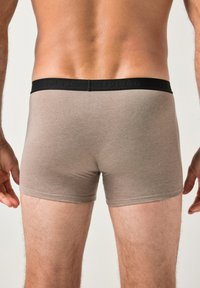Boxer cortos de algodón marrón con una cinturilla elástica negra que presenta una marca en relieve, diseñados para un ajuste ceñido y cobertura hasta la mitad del muslo.