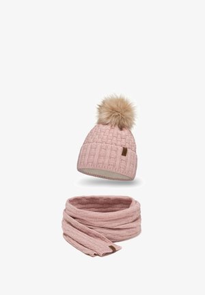 Un bonnet en tricot rose avec un pompon en fourrure sur le dessus et une écharpe en tricot assortie, tous deux présentant un motif texturé et une étiquette en tissu.