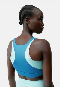 Blå og lyseblå sports-BH med et slankt design, med racerback-stil og glatt tekstur. To-farget fargeblokker på stoffet.