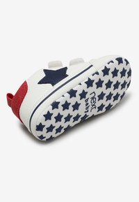 Scarpa da bambino in pelle bianca con accento a stella blu, tallone rosso e suola con stelle stampate. Chiusura con velcro e tomaia in tessuto per una facile vestibilità.