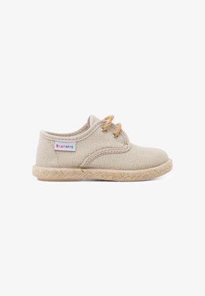 Zapato beige para niño pequeño con tejido entrelazado, dos ojales para cordones, suela texturizada y una pequeña etiqueta de tela colorida "Pisamonas" en el lateral.