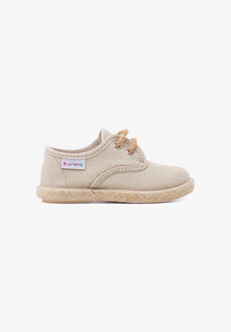 Chaussure beige pour tout-petit en tissu tissé, avec deux œillets pour lacets, semelle texturée et une petite étiquette en tissu colorée "Pisamonas" sur le côté.