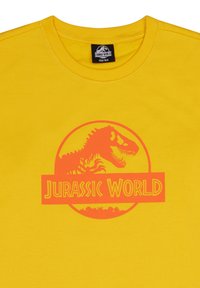 Camiseta de algodón amarilla con un gran logo en naranja de "Jurassic World" que incluye la silueta de un dinosaurio, diseño redondo y cuello acanalado.