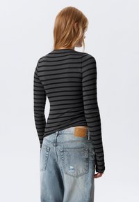 Long-sleeve black and gray striped top viewed from the back, paired with distressed light blue denim jeans, featuring a branded leather tag.