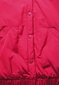 Veste rembourrée rose avec une texture douce, dotée de six boutons-pression et de deux poches latérales, resserrée à la taille pour un look ajusté.