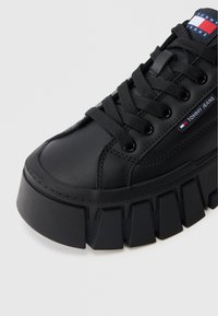 Schwarzer Ledersneaker mit einer dicken schwarzen Plateausohle, flachen schwarzen Schnürsenkeln, einem Markenetikett und einer glatten Textur.