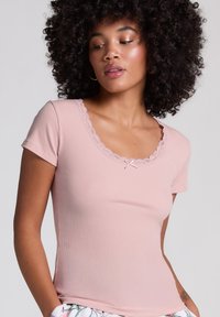 Ljusrosa figurnära T-shirt med korta ärmar, ribbad struktur, vågig spets vid halsringningen och en liten rosett i mitten.