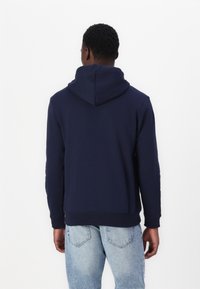 Sudadera azul marino con capucha ajustable, mangas largas y puños de canalé, fabricada en una tela suave, combinada con jeans de denim azul claro.