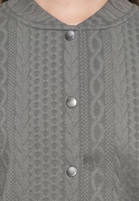 Cardigan en tricot gris à capuche, avec des motifs texturés et des boutons métalliques sur le devant.